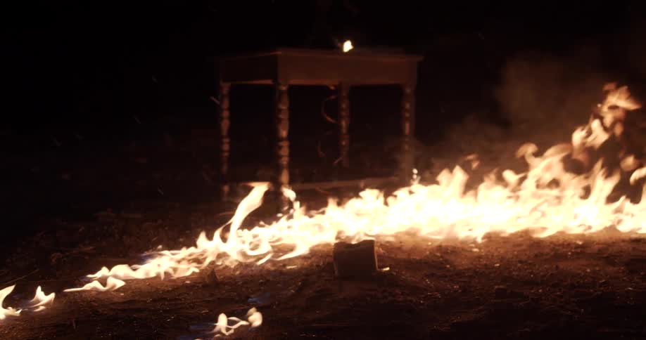 Fire burning outside at nighttime on the ground in front of a small wooden nightstand