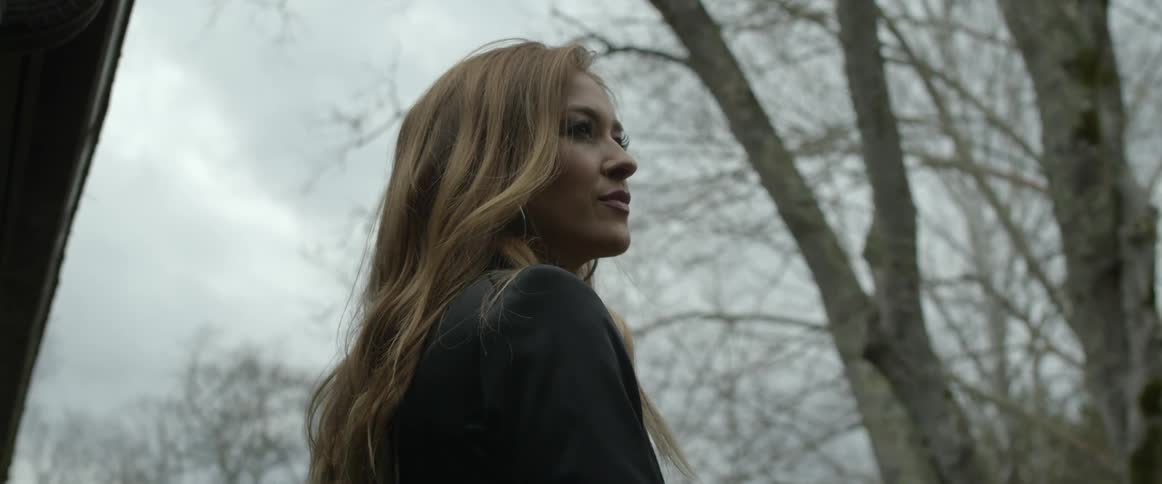 A woman standing next to trees without leaves looks off in to the distance