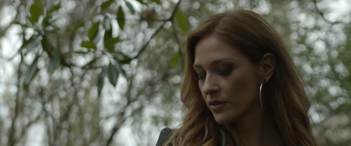 A woman with makeup and earrings walking with trees the sky and clouds in the background