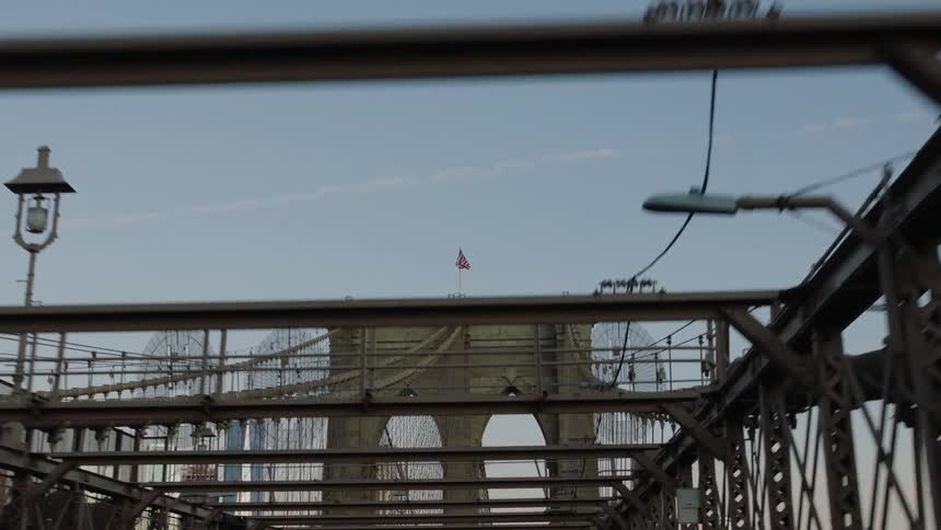 A bridge with an american flag above with skyscrapers the sky and clouds in the background