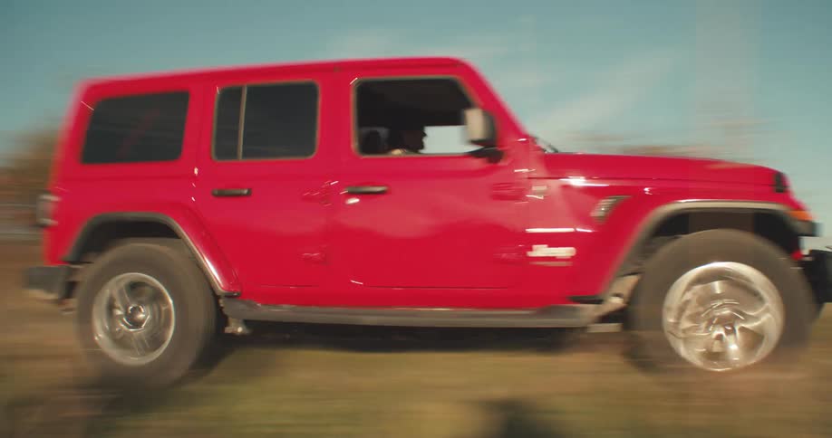 A sport utility drives quickly on a road next to a field