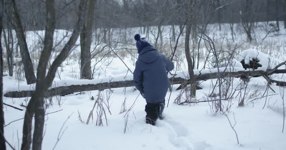 A young child walks through a snow covered forest