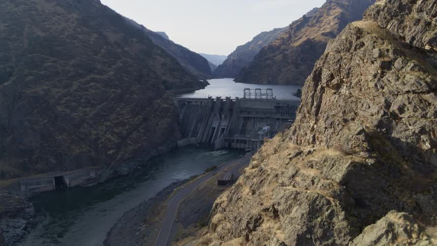 Flying along the edge of a deep river canyon where a hydro dam is generating power