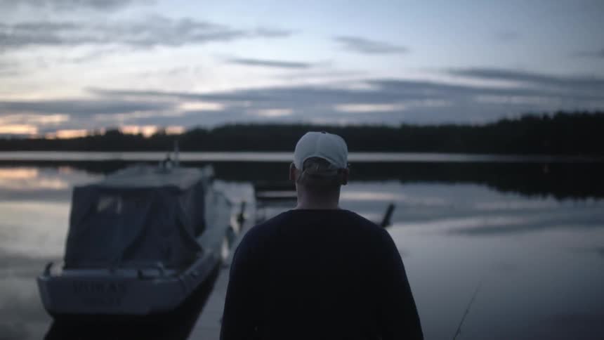 A man carrying a fishing pole walks onto a pier and towards a boat at dusk