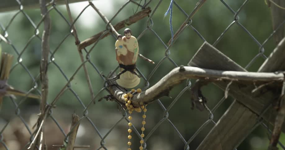 A branch and small statue next to a chain link fence