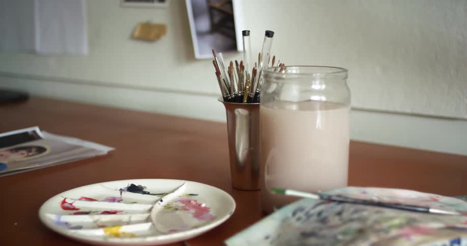 Dirty paint palettes and paper adorn a long wooden desk