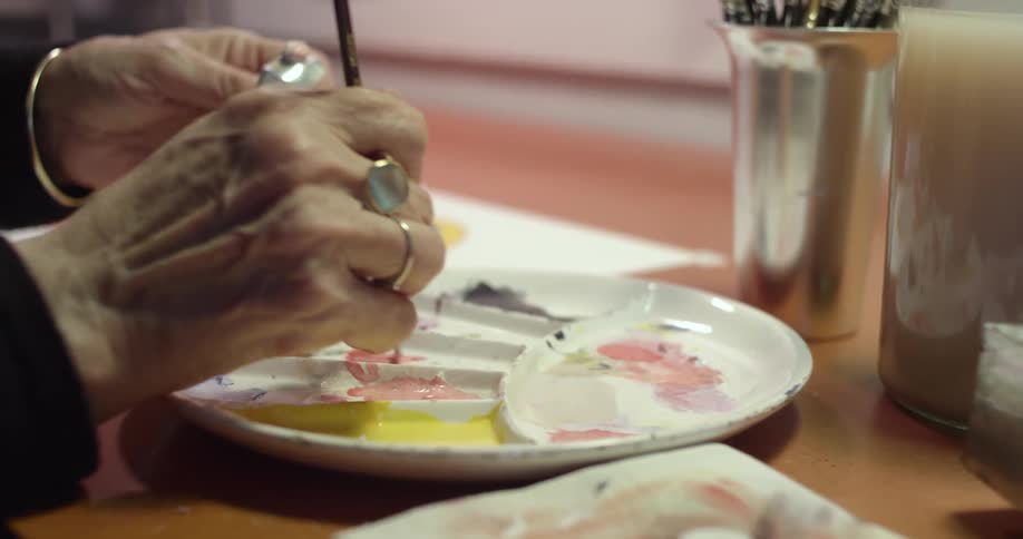 A person in a room using a paint brush to paint a picture on a paper on a table