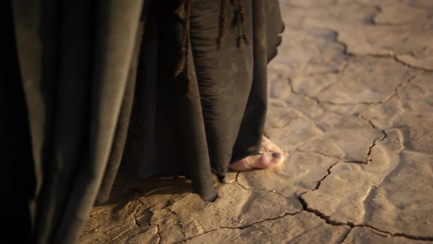 A person in long dark robes walks in the sand