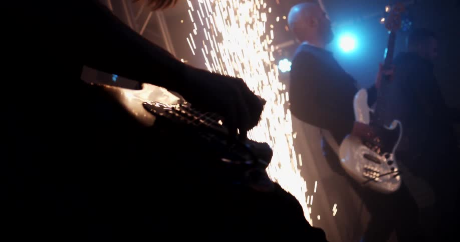 A band plays on stage as sparks fly and lights glow