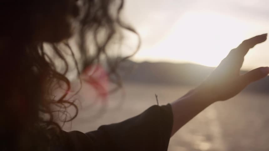 A woman reaches her arm out and stands up in the desert