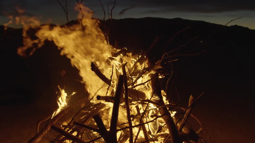 A bonfire blazes outside in front of a large hill