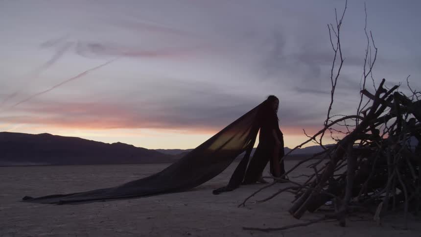 A woman that is walking on a dry lake bed in a dress