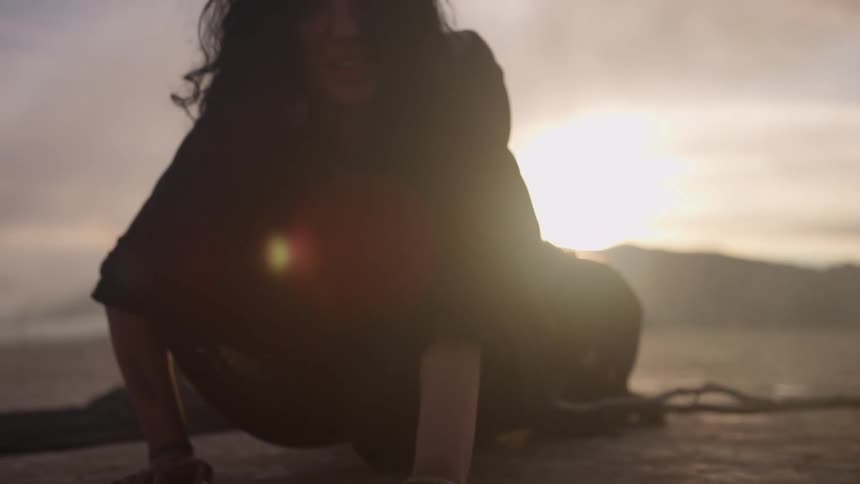 A woman in a flowy black dress crawls through the desert on her hands and knees