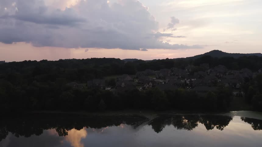 A pond near a hillside neighborhood reflects the surrounding trees and sky