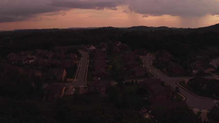 A neighborhood with houses trees and roads with the sky and clouds in the background