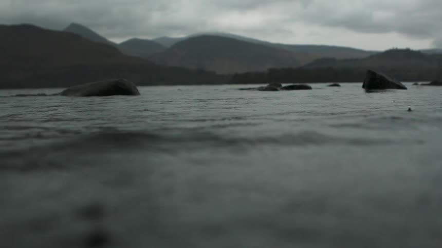 A body of water with a mountainous shoreline on a cloudy day