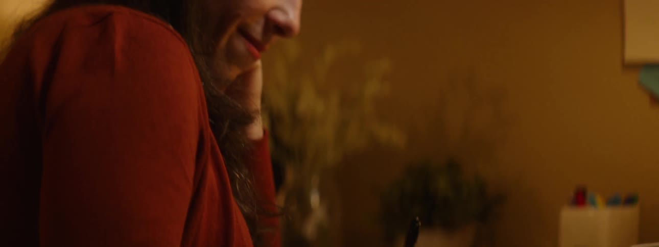 A woman sitting on a desk writing on a book with a pen