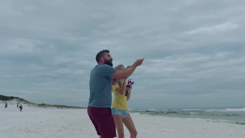 A man and a woman flying a kite on a beach with the sky and clouds in the background
