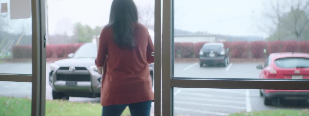 A woman carries a two cardboard boxes stacked on top of each other out the front door of a store