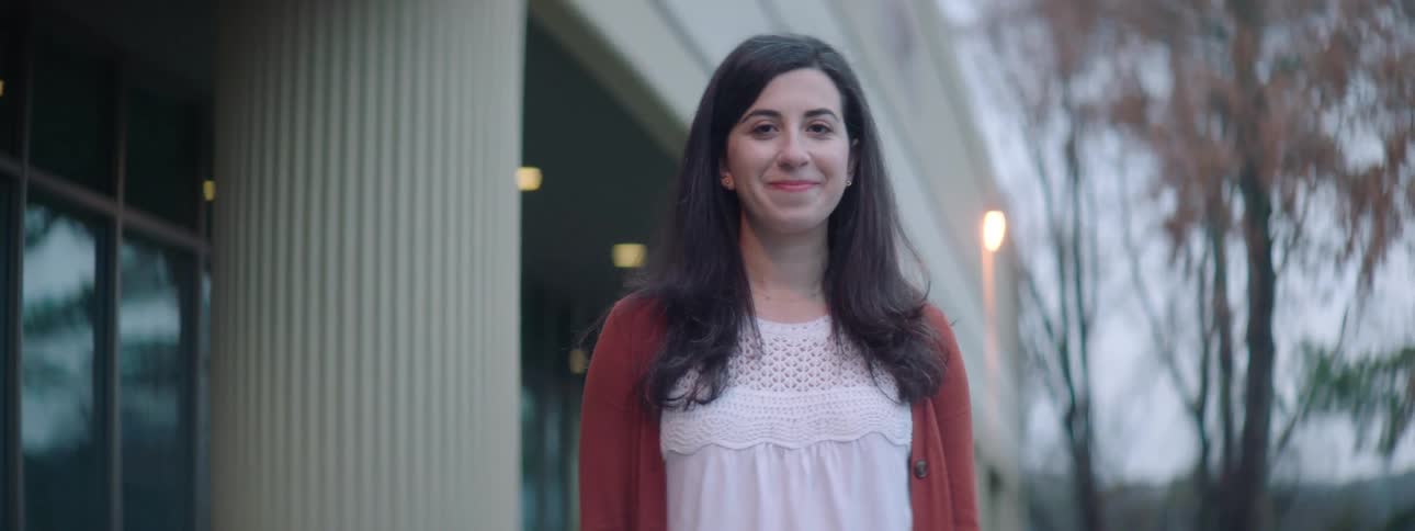 Long haired woman standing outside a building turns around to look at the camera