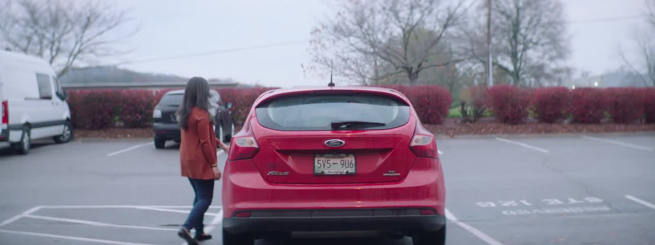 A woman closes the trunk of her car with boxes inside then opens the driver side door and gets in