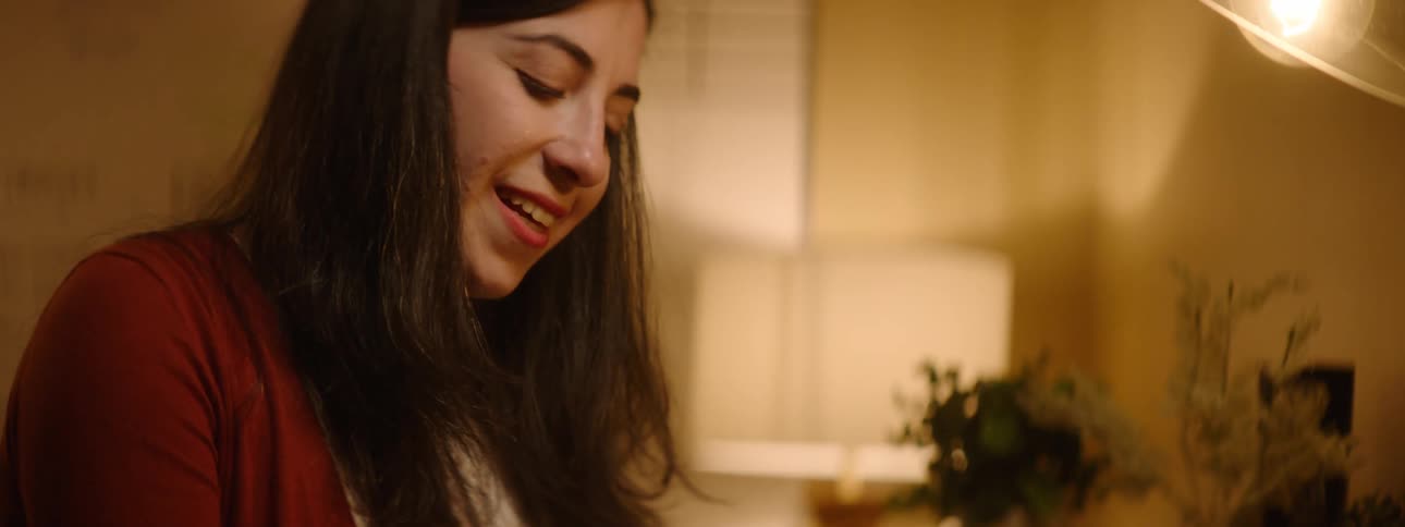 A woman smiles and looks up as she thinks while writing at her desk