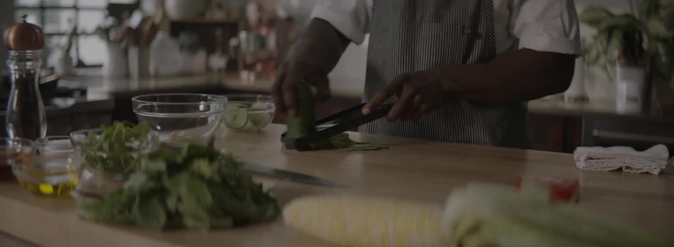 A chef works at a counter in his kitchen slicing cucumber