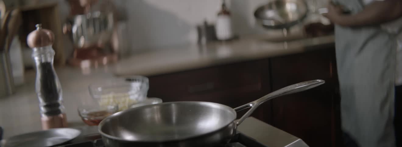 A cook places pans on a stovetop