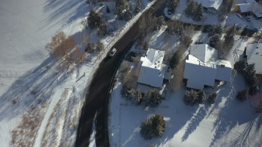 A car travels on a rural road past snow covered homes