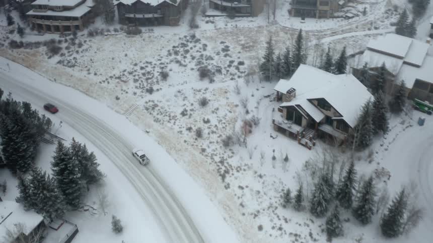 An aerial view of cars driving on a snowy road near houses in a neighborhood