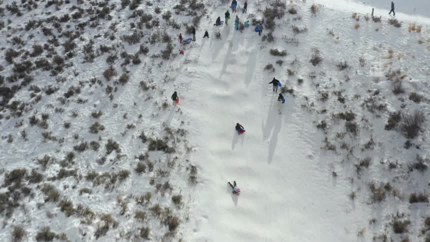 A group of people having fun riding ice slides on the side of a snow covered hill at winter
