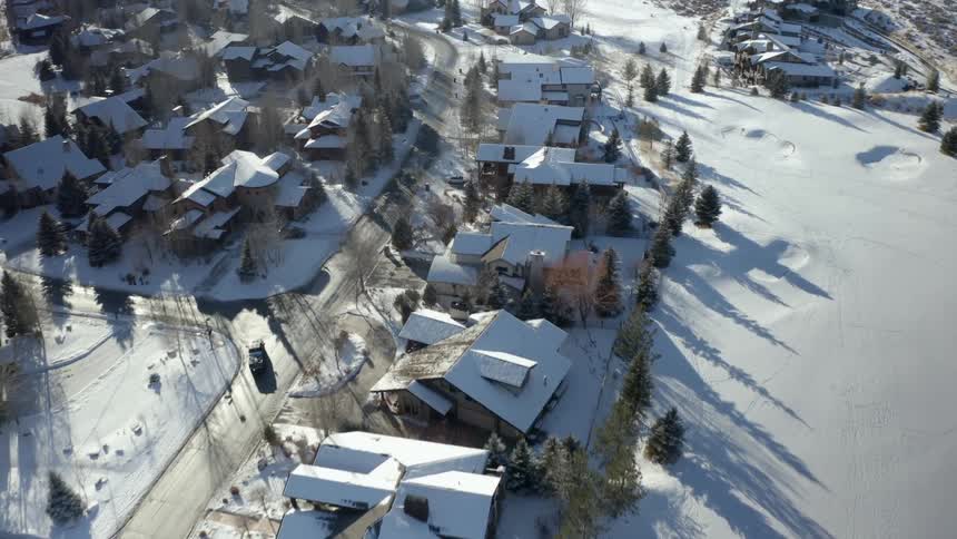 A vehicle is driving down a road in a town with a fresh snowfall