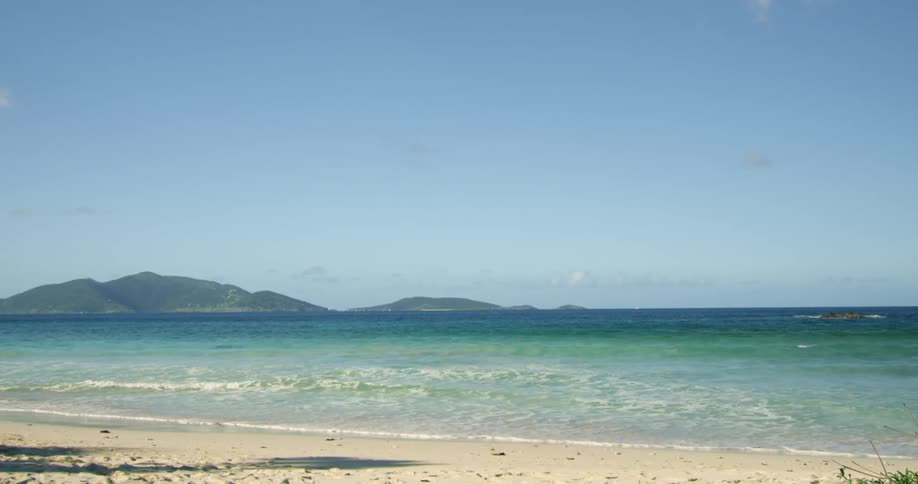 Waves rolling in on beach with mountains in the distance