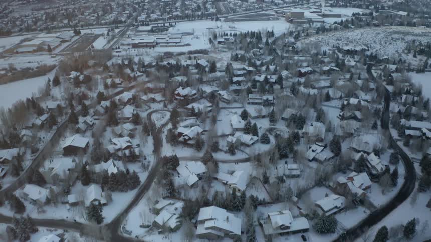 An aerial view of houses in a snow covered neighborhood with hills in the background