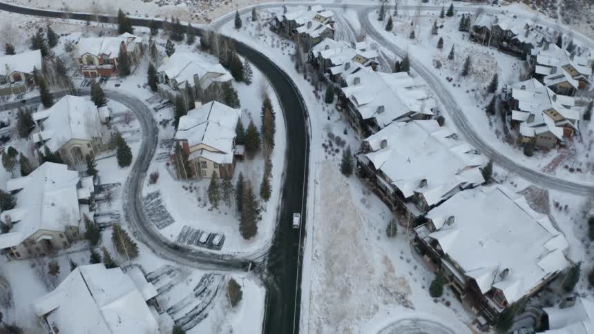 A vehicle travels along a road through snowy neighborhood of large houses