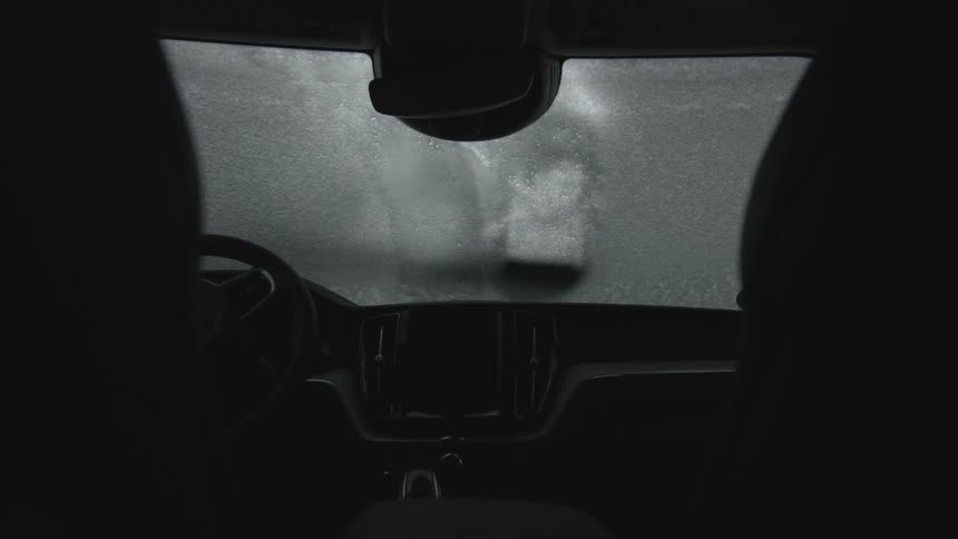 A person brushes snow off a car windshield
