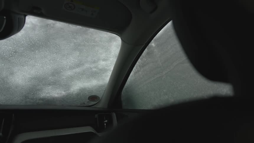 A person wipes the snow from windshield of a vehicle on a winter day