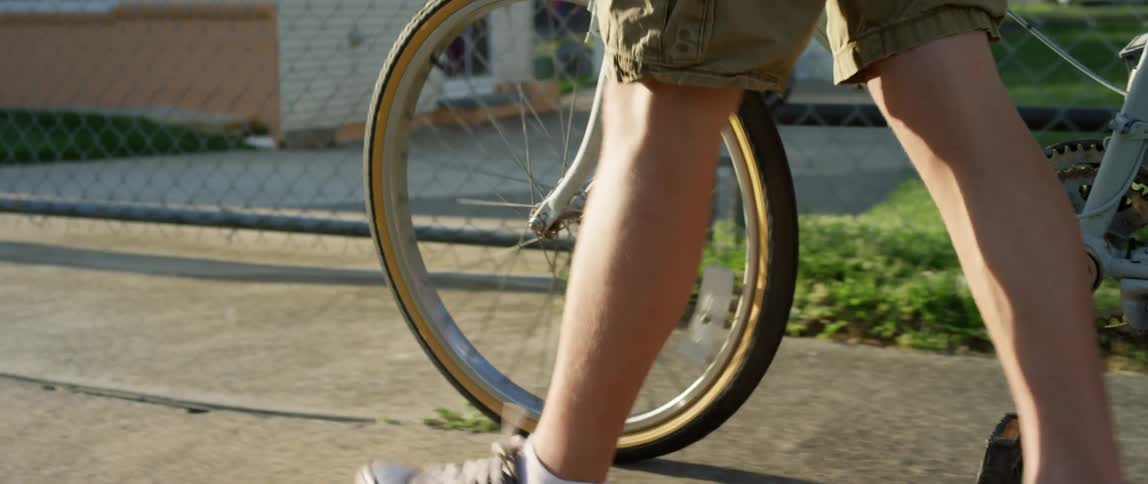 A person pushes a bicycle along the sidewalk of a residential neighborhood during the day