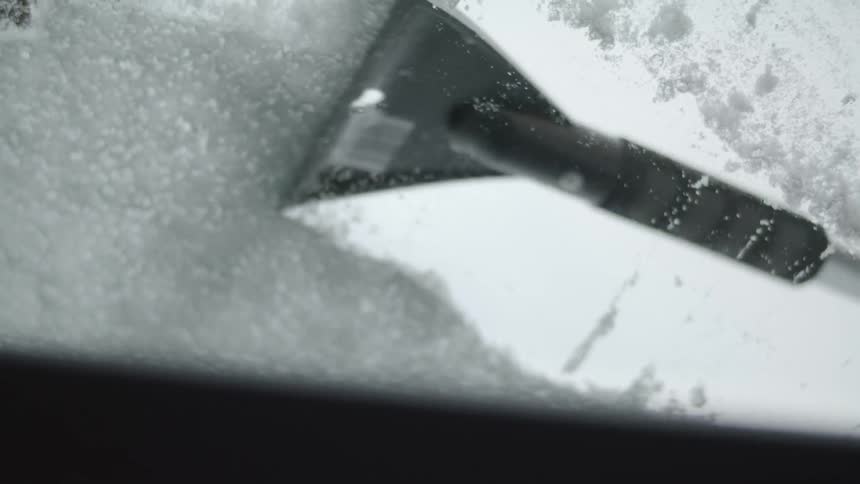 A snow scraper scaping snow off of a vehicle windshield