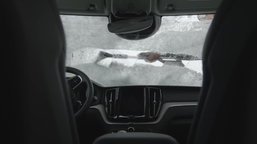 A vehicle with a steering wheel with a person with a tool removing snow from the windshield