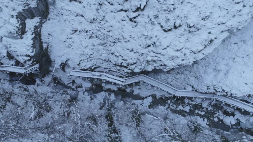 An aerial view of a snow covered mountain with a river in the valley and a broken pathway along the mountain