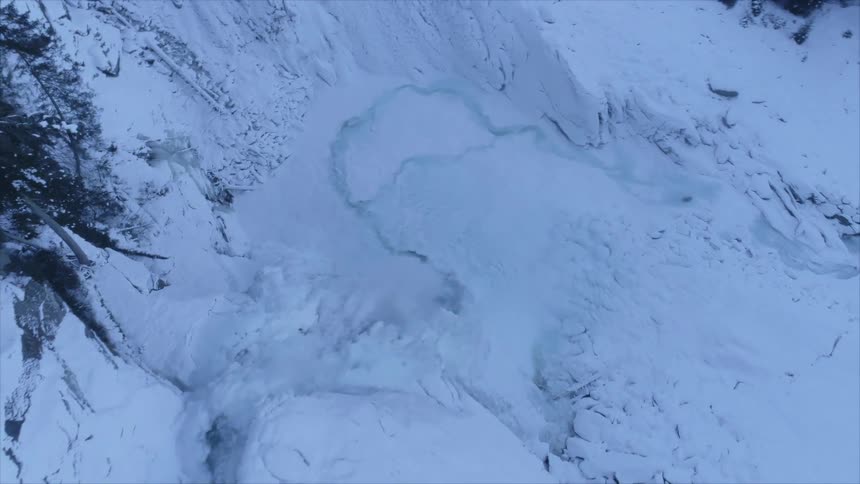 A waterfall down a snowy cliff into a valley covered in snow and ice