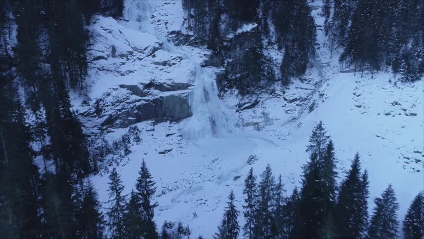 Water and snow flow down a rock face in a landscape of evergreen trees and snow