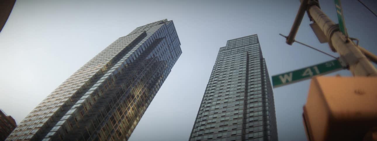 A city street with signs and a crosswalk traffic light with skyscrapers the sky and clouds in the background