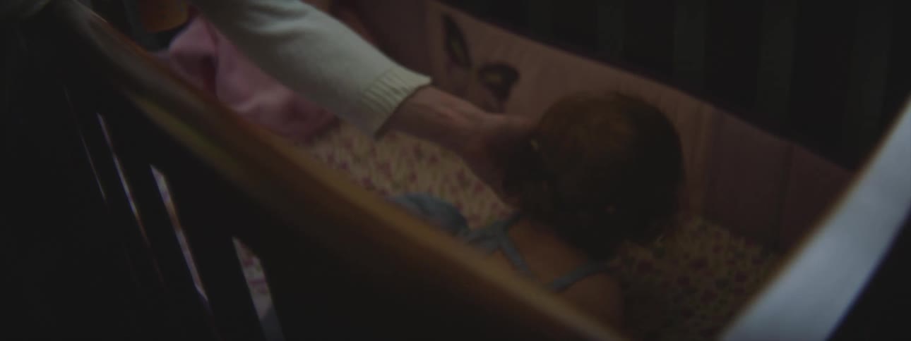 A baby lies down in her crib as her mother rubs her back