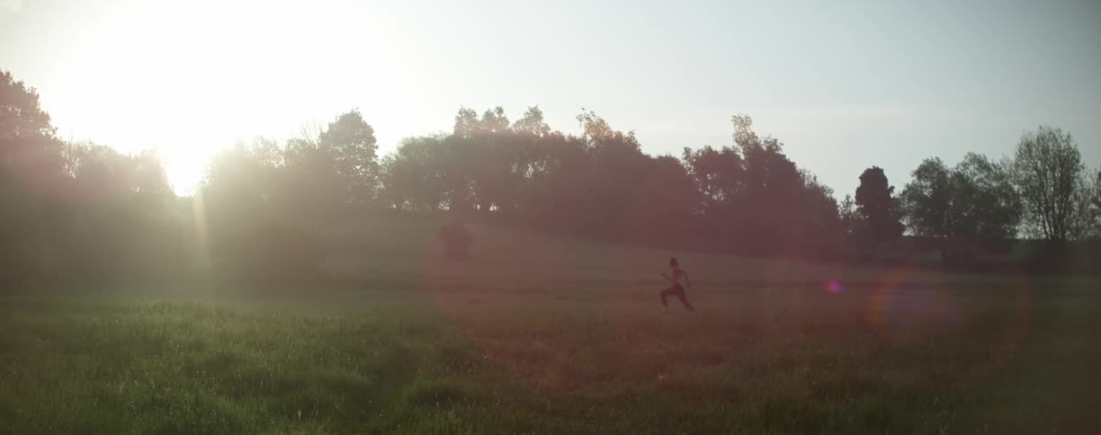 Shirtless man running on a green grass field at sunset