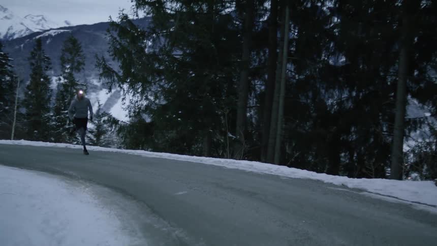 A man runs along a road off the coast with mountains in the background