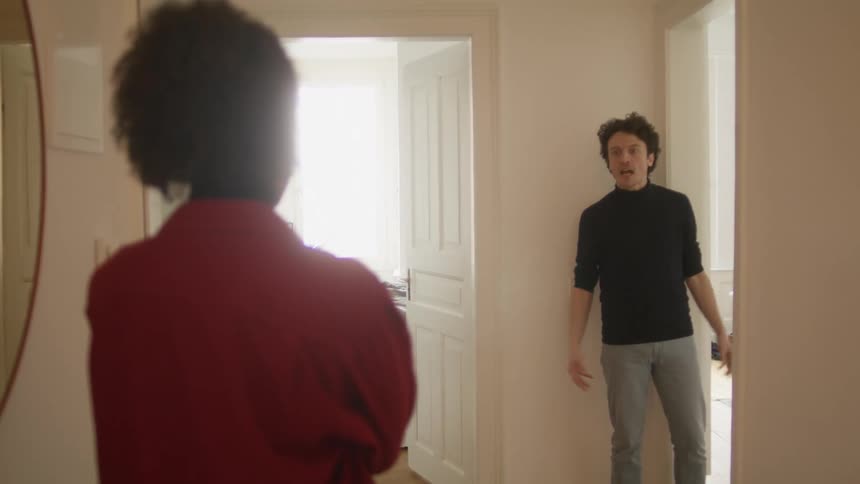 A man exits a room to yell at a woman standing in the corridor before walking off into another room