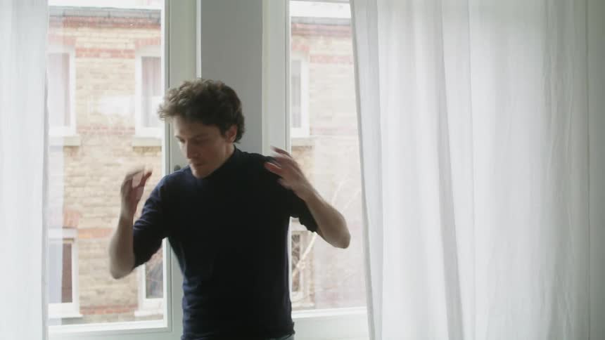 A man points and gestures with his hands as he stands by a window and yells and argues