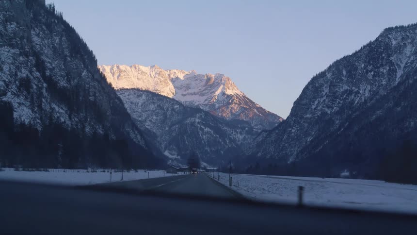Traffic moves along a road through a snowy valley between mountains on a clear day
